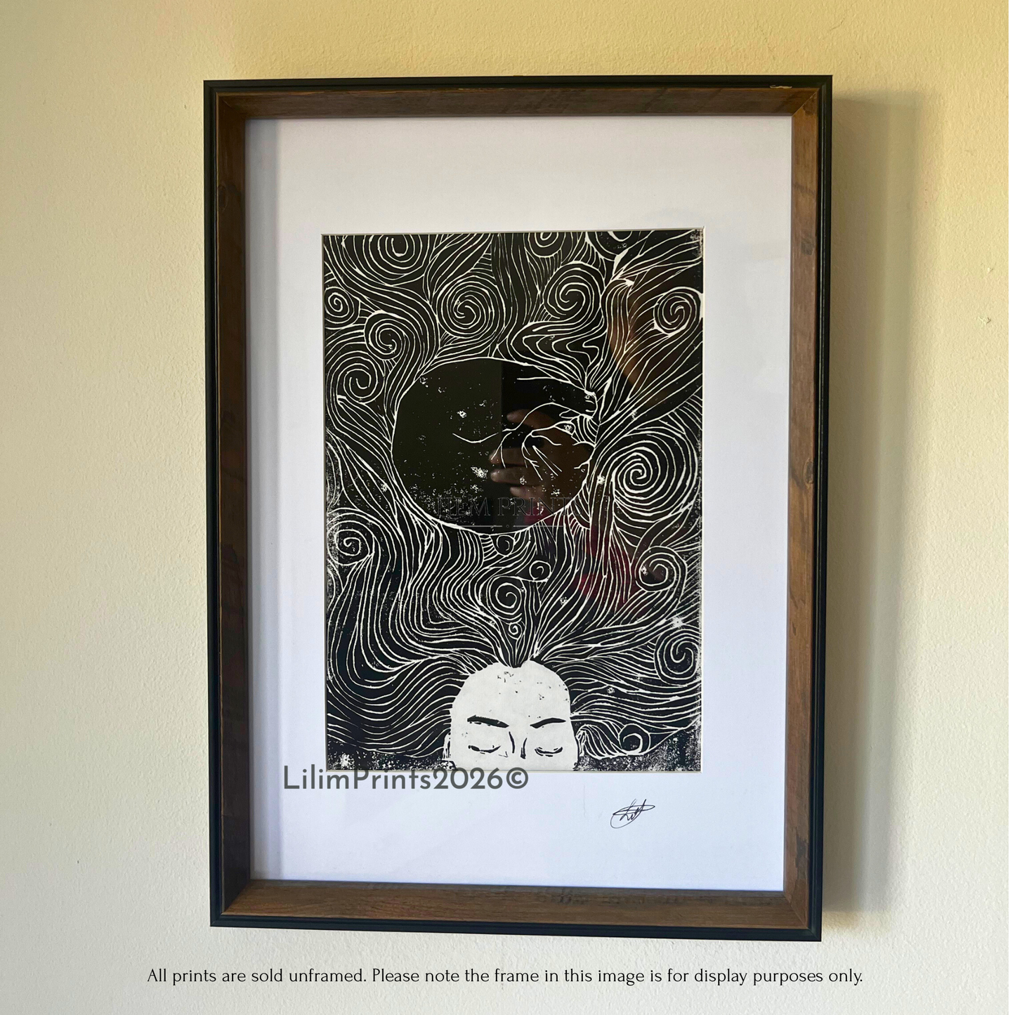 A lino print image in a frame hung on the wall. a sleeping woman and a cat curled in her swirling hair. 